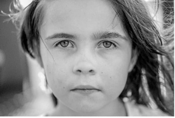 A black-and-white close-up portrait of a young girl with a serious expression, gazing directly into the camera