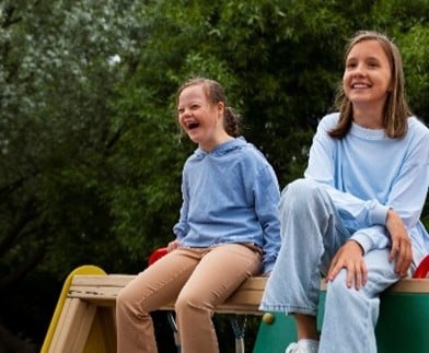 Two children sitting outdoors, laughing and enjoying themselves