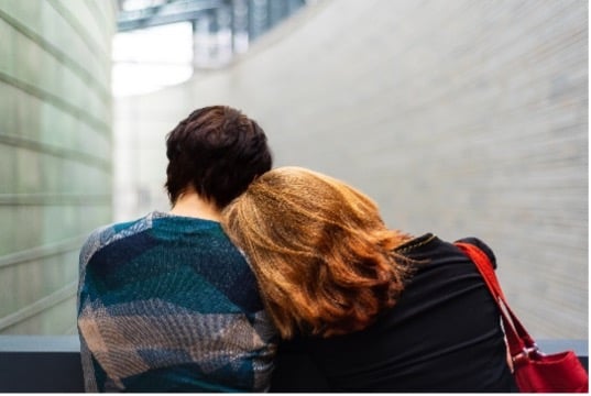 Two people sitting closely together, one person resting their head on the other's shoulder